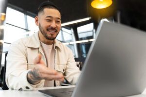 homem sorrindo de frente ao computador, conversando com alguém de maneira online